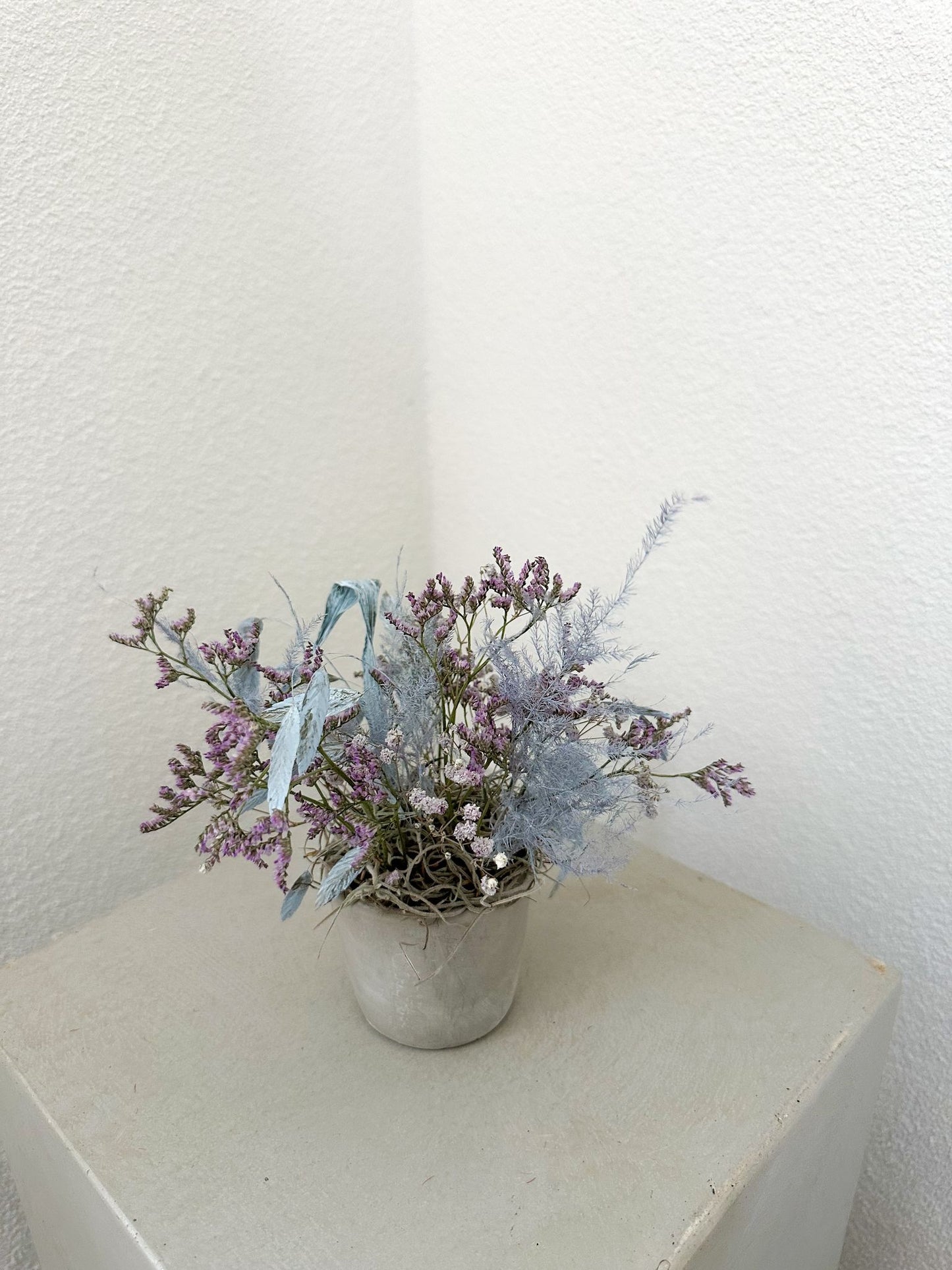 Blumengesteck mit lavendelfarbenem Statice, hellblauem Farn und Schleierkraut in grauer Vase – modern und reduziert.