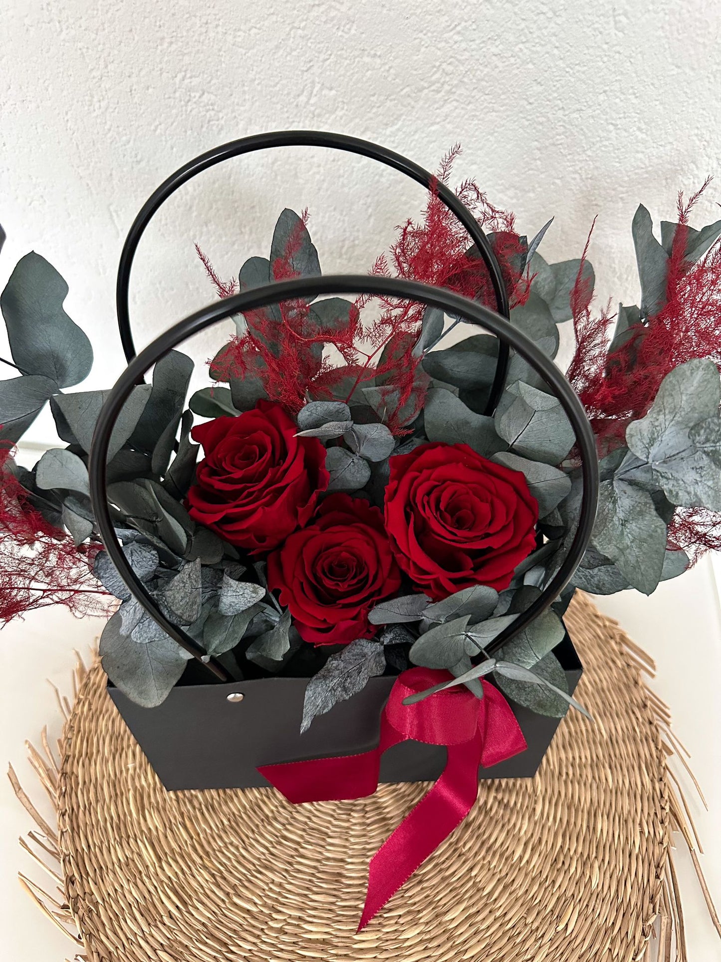 Nahaufnahme der Blumentasche mit leuchtend roten Rosen und elegantem Eukalyptus in einer schwarzen Tasche mit Griff.