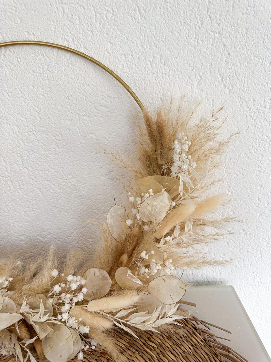 Detailansicht des Daniela Hoops an einer weißen Wand, mit einem Blick auf die kunstvolle Anordnung der Trockenblumen – Pampas, Schleierkraut, Lagurus, Lunaria – an einem eleganten goldenen Ring, der Stil und sanfte Naturästhetik in die Raumdekoration bringt.