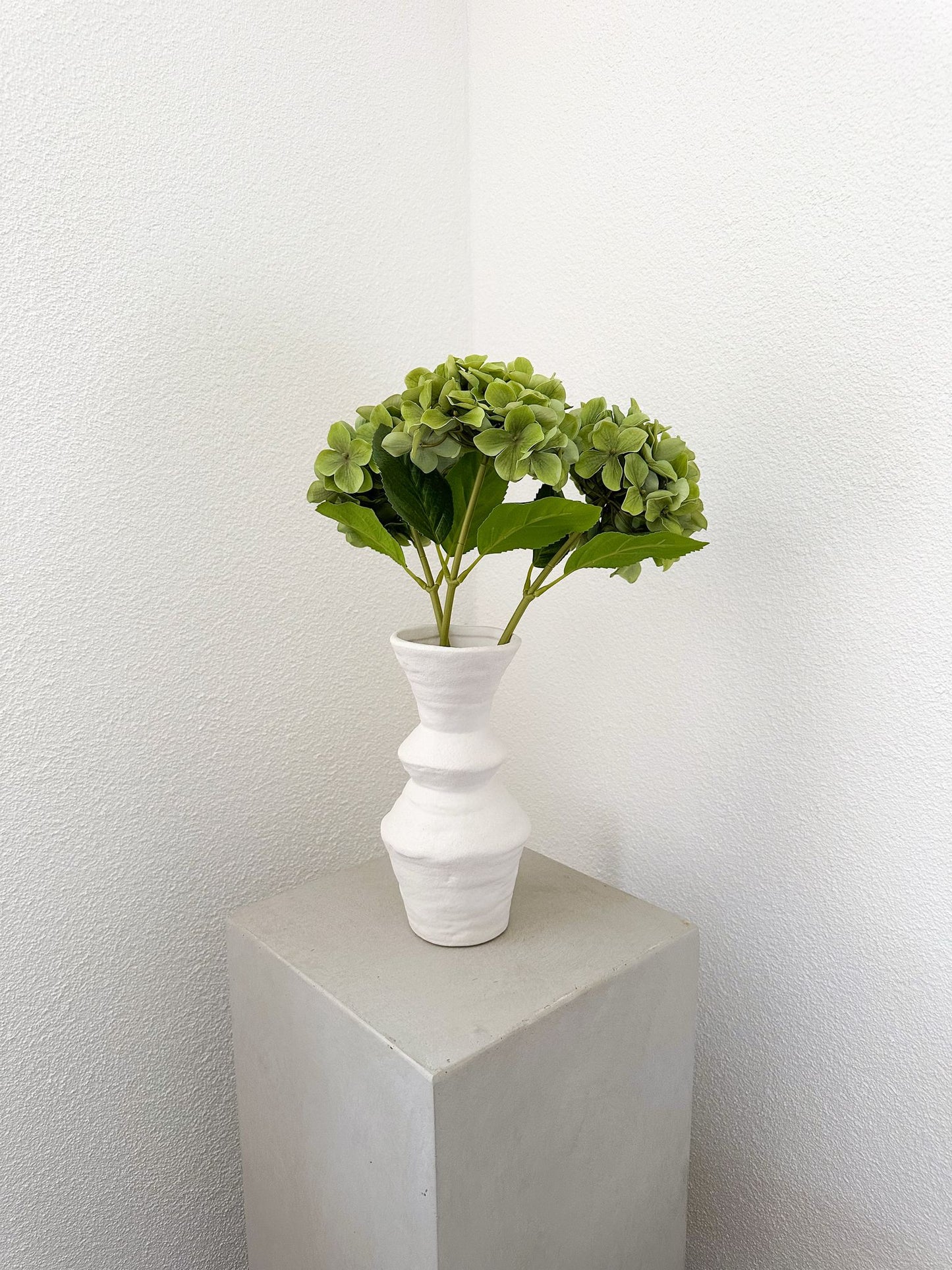 Minimalistisches Arrangement mit drei grünen Kunsthortensien, dekorativ platziert in weisser Vase zur Inspiration (nicht im Lieferumfang).
