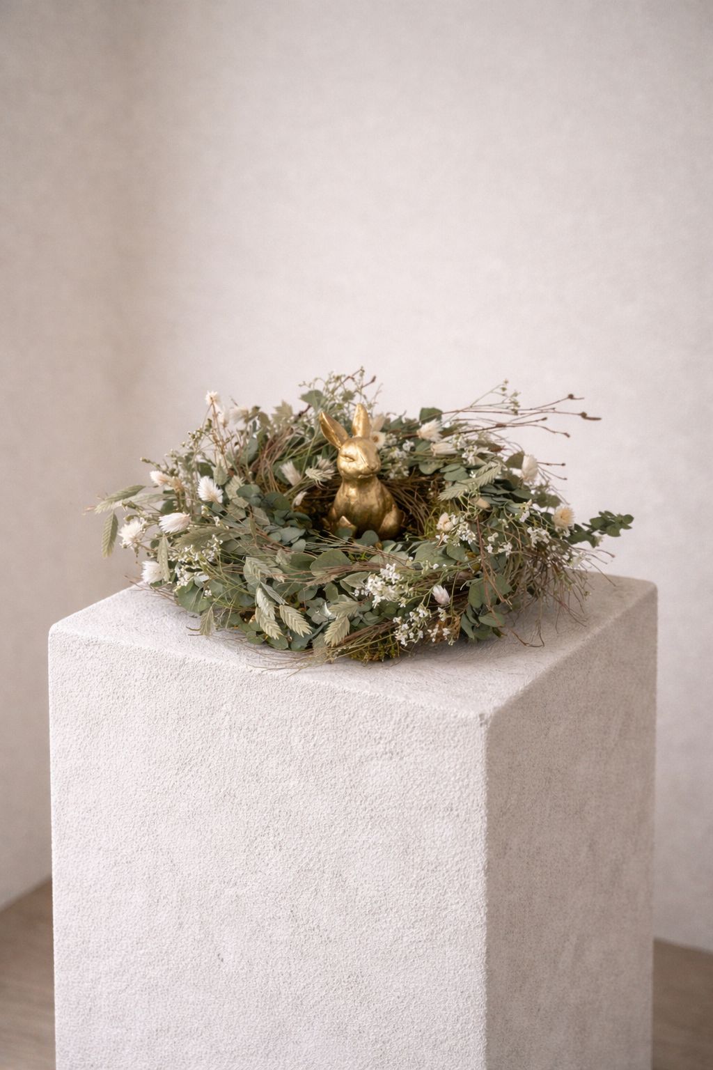 Osternest aus Trockenblumen mit Eukalyptus, Limonium und Chasmanthium mit goldenem Osterhasen als Tischdekoration.