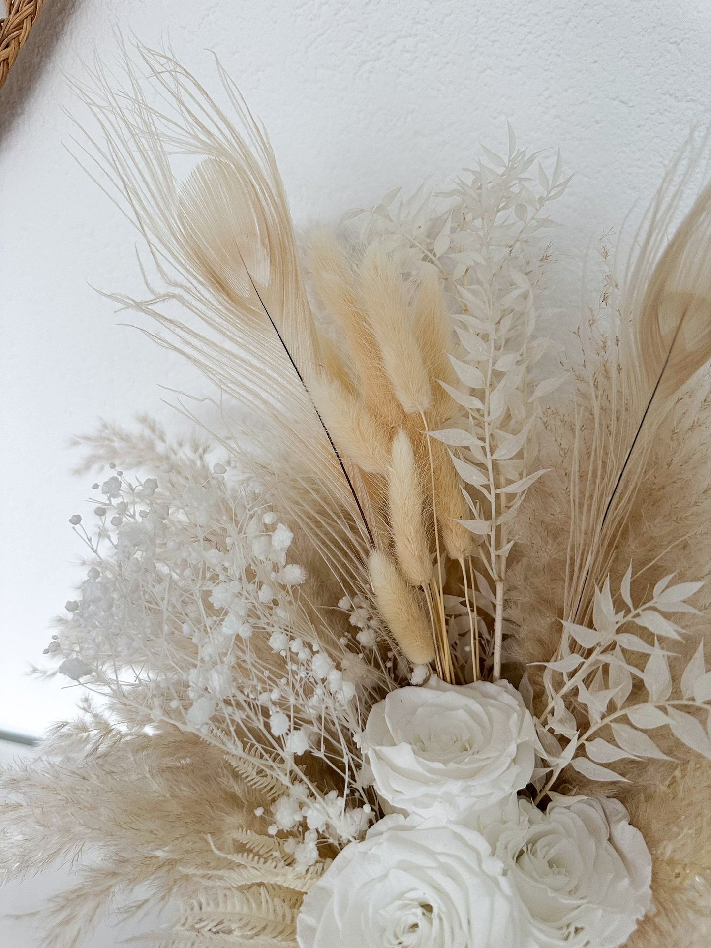 Nahaufnahme eines eleganten Trockenblumenstrausses mit Pampasgras, stabilisierten Rosen, Schleierkraut, Ruscus, Lagurus, Helechi und Pfaufedern in Creme- und Beigetönen.