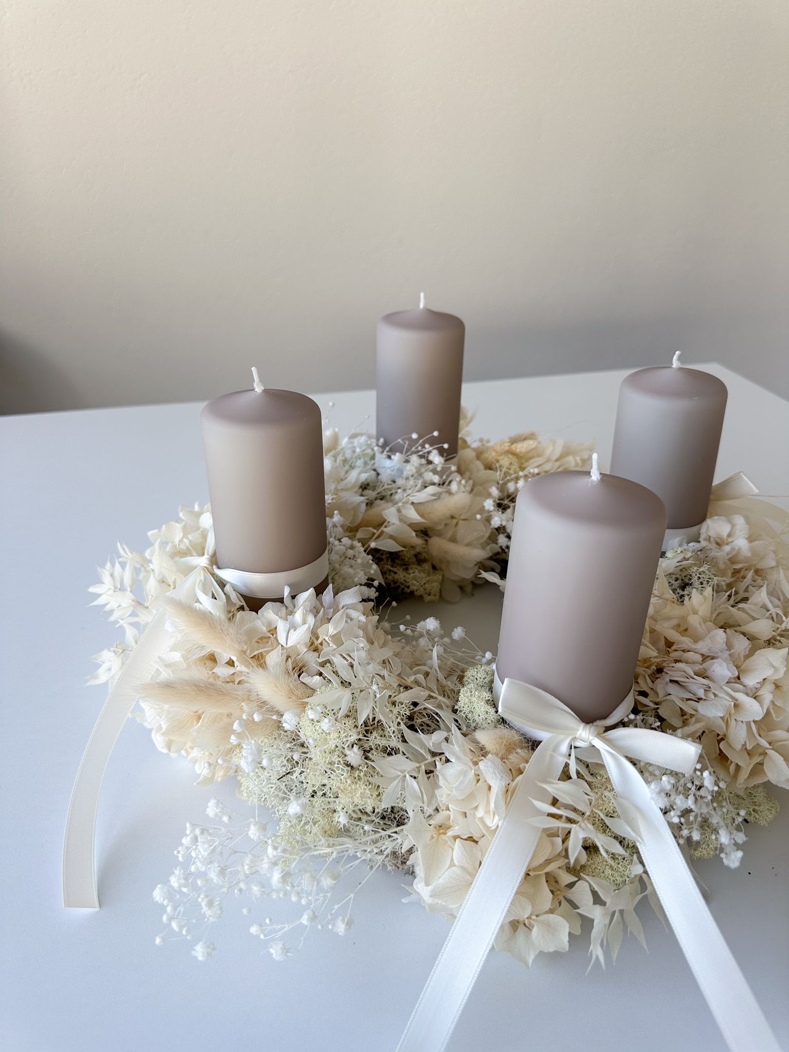 Adventskranz Sonja mit vier Stumpenkerzen in Steinfarbe und weissen Satinbändern – elegante Tischdekoration.