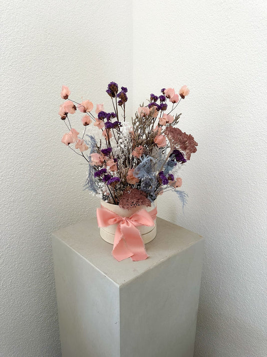 Trockenblumenbox mit violettem Limonium, rosa Bougainvillea und Schleierkraut, dekorativ in roséfarbener Stoffbox mit Schleife.