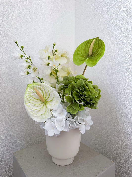 Kunstblumenstrauss aus der Seitenansicht, bestehend aus weisser Anthurie, grüner Hortensie, zarten Orchideen und weisser Campanula, in einer minimalistischen weissen Vase.