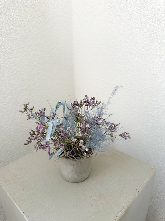 Blumengesteck mit lavendelfarbenem Statice, hellblauem Farn und Schleierkraut in grauer Vase – modern und reduziert.