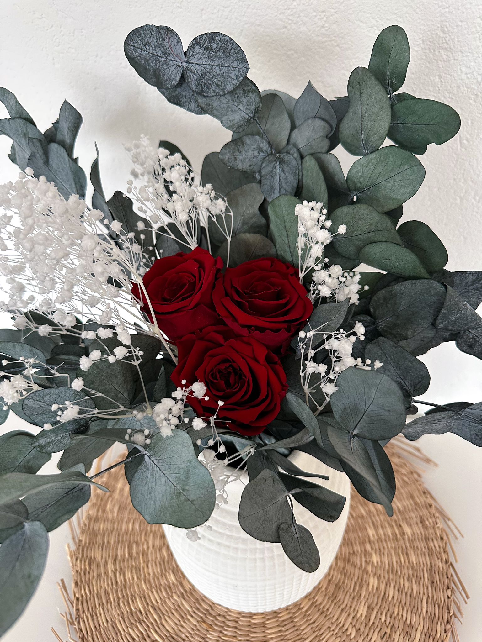 Der Emina Bouquet in einer weißen Vase, perfekt arrangiert mit drei Rosen, Schleierkraut und Eukalyptus.