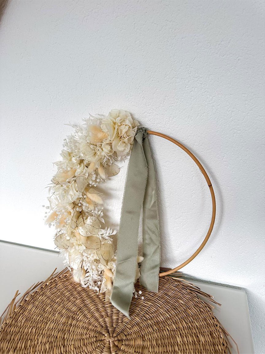 Handgefertigter Gloria Flowerhoop mit Hortensien und grünem Band auf einem Weidenkranz, präsentiert auf einem Rattantisch.