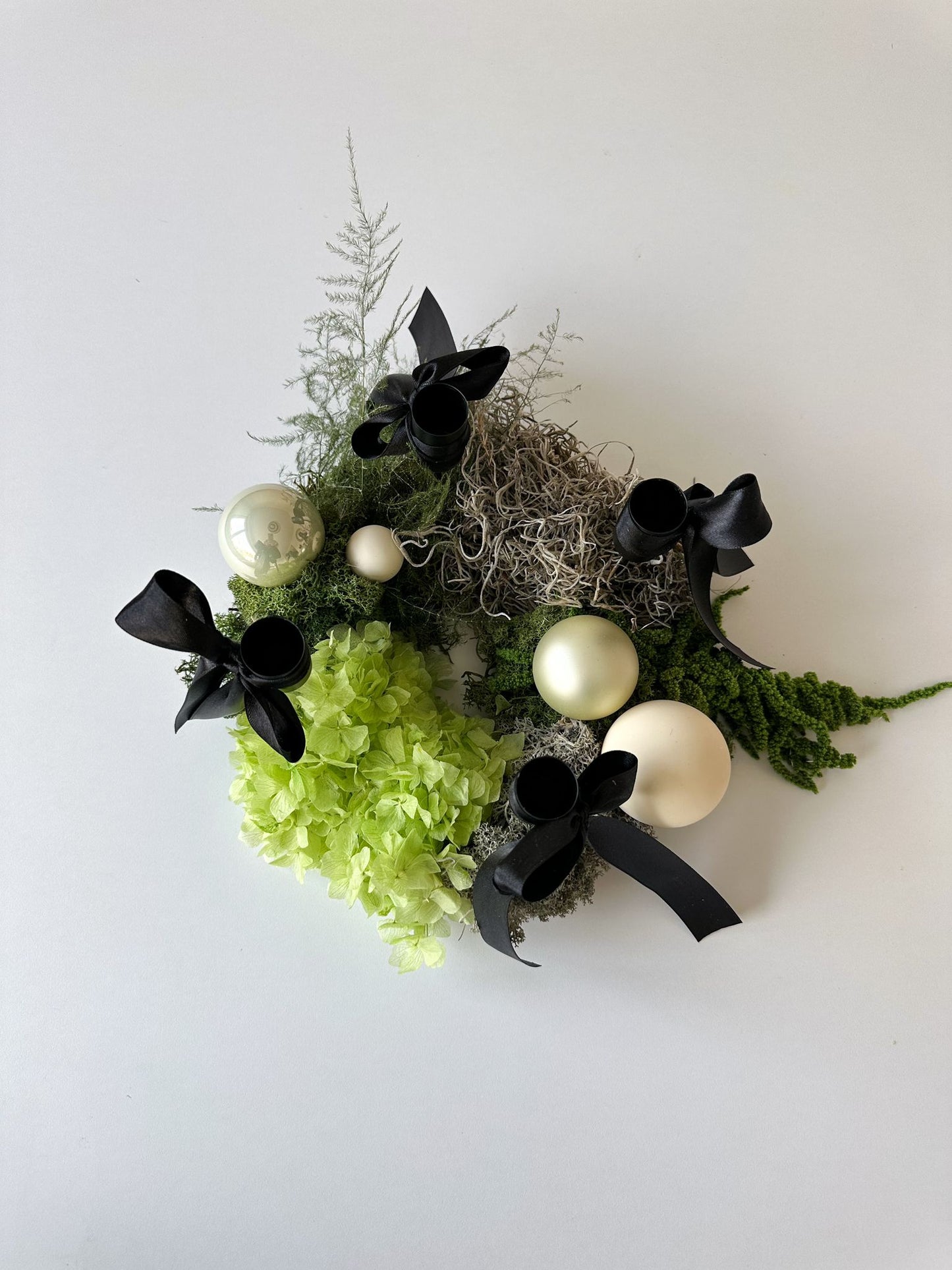 Adventskranz Amire mit eingesetzten weissen Stabkerzen und schwarzen Schleifen – modernes Adventsdesign für stilvolle Wohnräume.