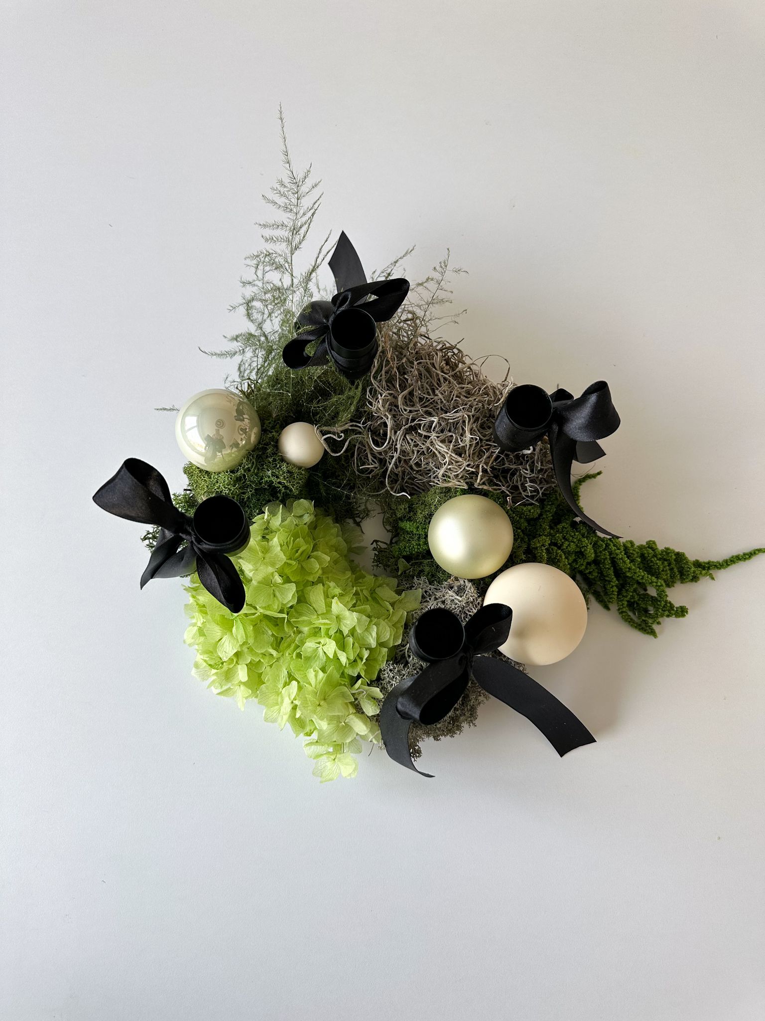 Adventskranz Amire mit eingesetzten weissen Stabkerzen und schwarzen Schleifen – modernes Adventsdesign für stilvolle Wohnräume.