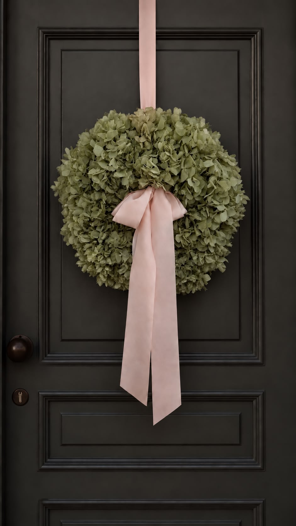 Hortensienkranz Iced Green mit rosa Schleife an einer dunklen Haustür
