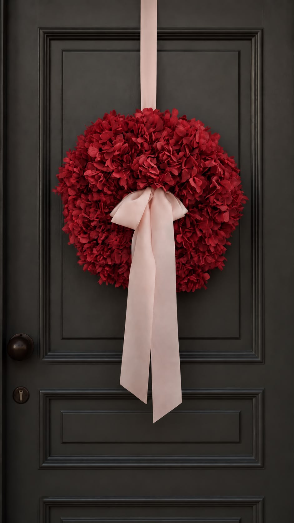 Roter Hortensienkranz mit rosa Schleife an einer dunklen Haustür